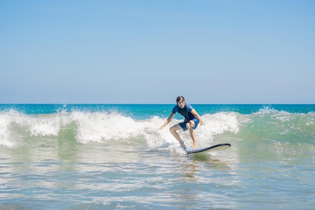 Young man, beginner Surfer learns to surf on a sea foam on the Bali island.