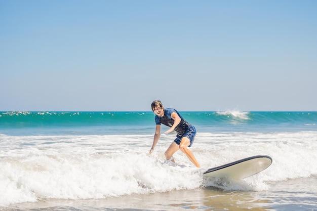 Young man, beginner Surfer learns to surf on a sea foam on the Bali island.