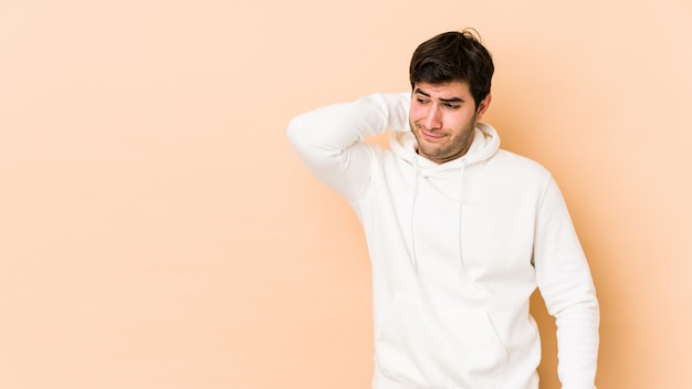 Young man on beige wall touching back of head, thinking and making a choice.