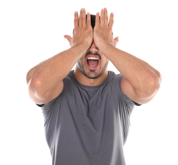 Young man being blinded and covering eyes with hands on white background