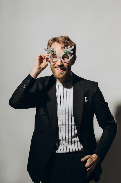 Young man in black jacket with party glasses on color background