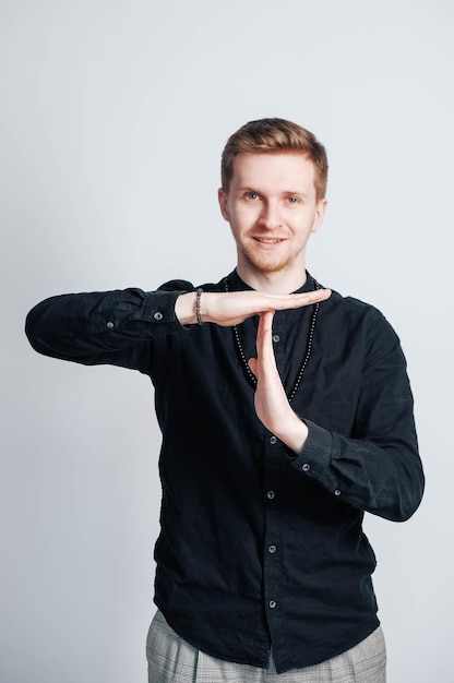 Young man in a black shirt shows a time out sign with his hands on a white background