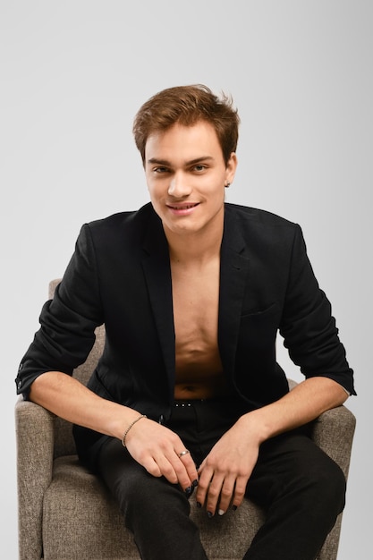 Young man in black suit siting in an armchair in the studio