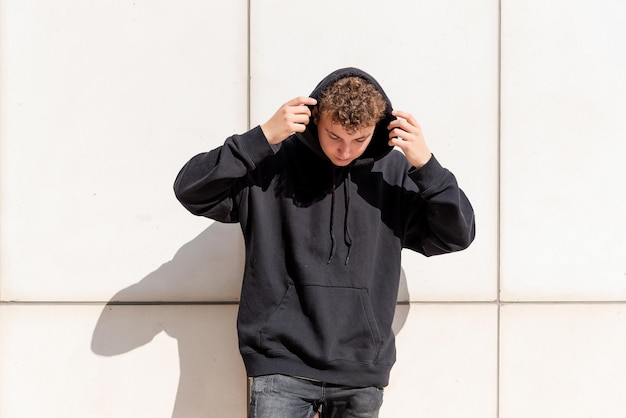 Young man in black sweatshirt putting his hood up on the outside and looking down