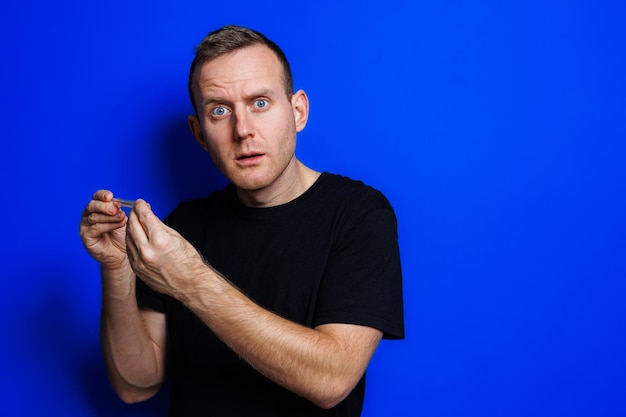 A young man in a black Tshirt on a blue background stands with a thermometer in his hands An increase in body temperature feeling sick Weakened immunity Selective focus