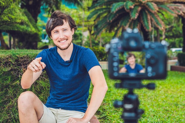 写真 若い男のブロガーが公園でカメラの前でビデオを記録します