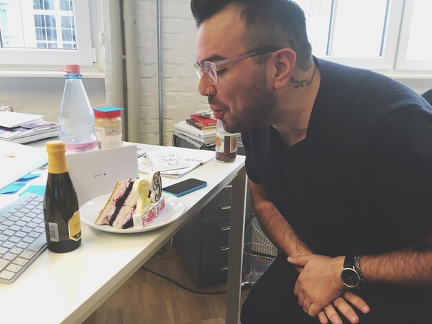 Photo young man blowing birthday candles at table in office