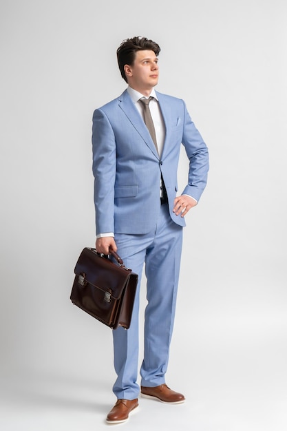 青いビジネス スーツの白いシャツと革のブリーフケースとネクタイを着た若い男