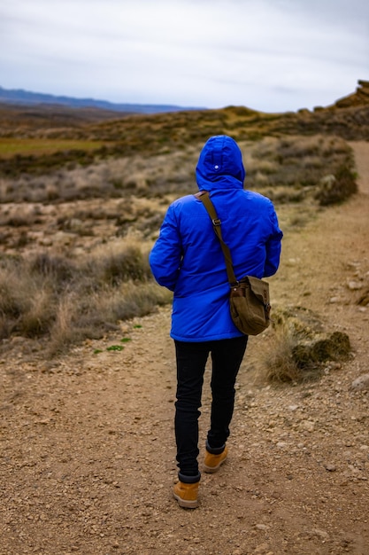 A young man in a blue coat and brown bag is looking out over the desert horizon Bardenas Reales Navarra Spain