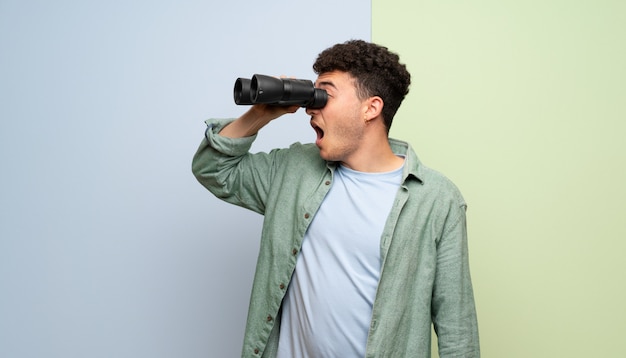 Young man over blue and green  and looking in the distance with binoculars