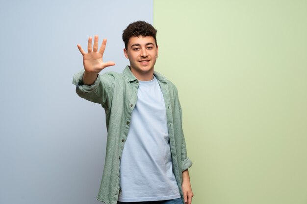 Young man over blue and green wall counting five with fingers