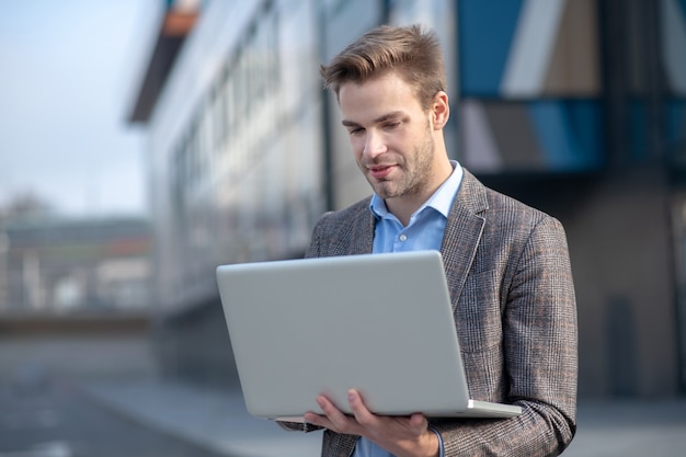 Giovane uomo in una camicia blu in possesso di un computer portatile in piedi accanto al centro business