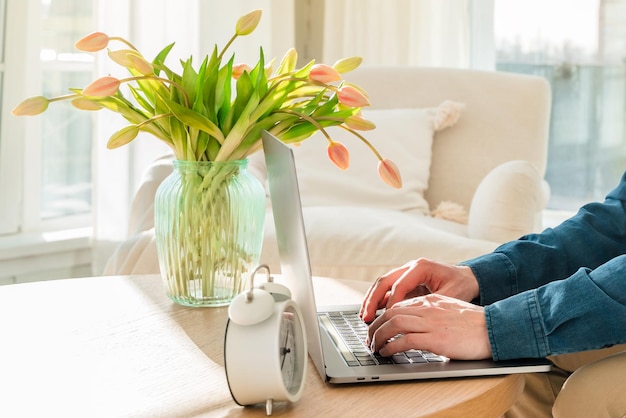 A young man in a blue shirt is working with a laptop while sitting on the couch at home