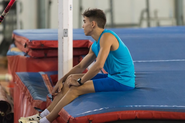 Young man in blue shirt sitting on the mat in the sports stadium