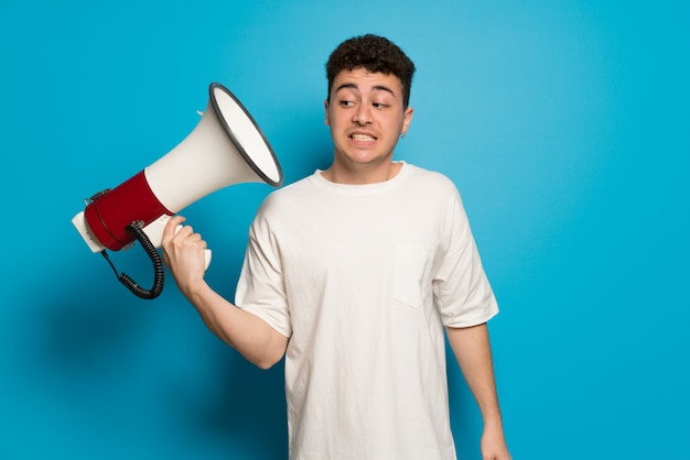 Young man over blue taking a megaphone that makes a lot of noise