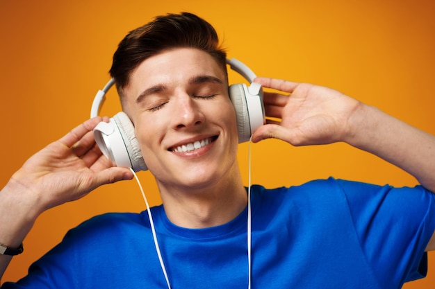 Молодой человек в синей футболке слушает музыку в наушниках на желтом фоне