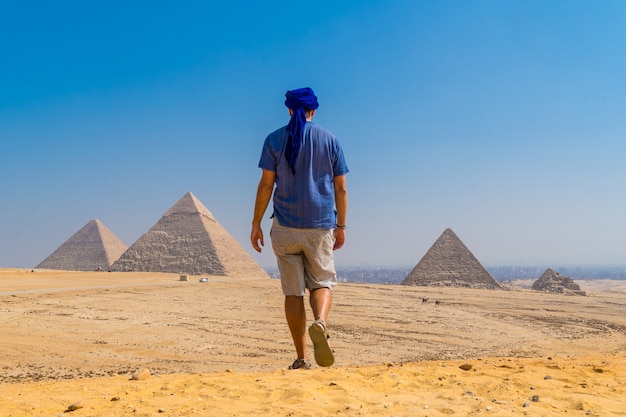 Un giovane con un turbante blu che cammina accanto alle piramidi di giza, il più antico monumento funerario del mondo. nella città del cairo, in egitto