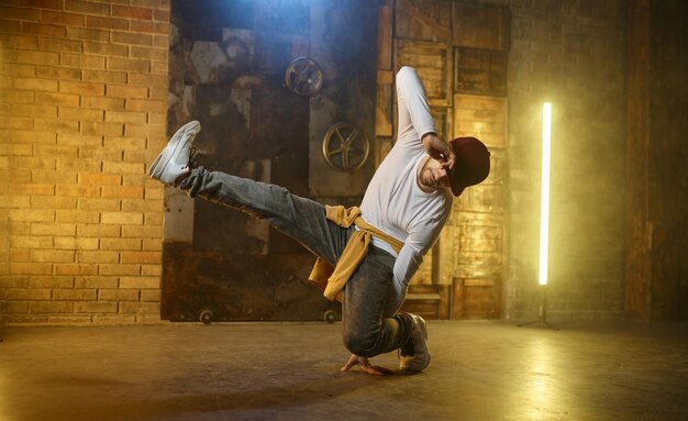 Young man breakdancer. Active stylish guy hip hop dancer training or performing over loft studio background