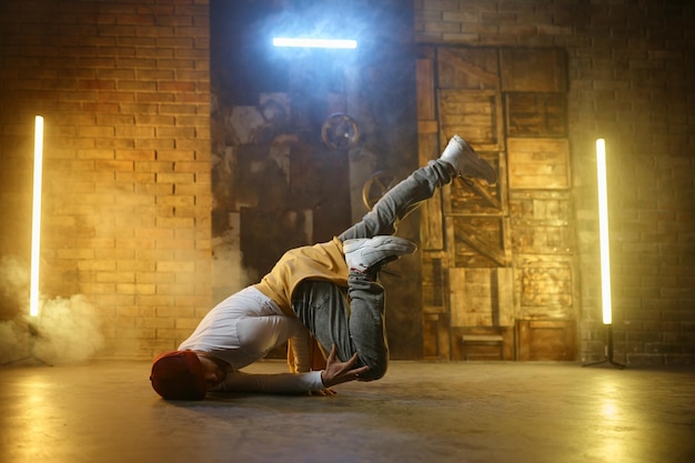 Young man breakdancer. Active stylish guy hip hop dancer training or performing over loft studio background