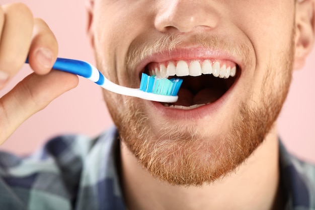 Young man brushing teeth on color