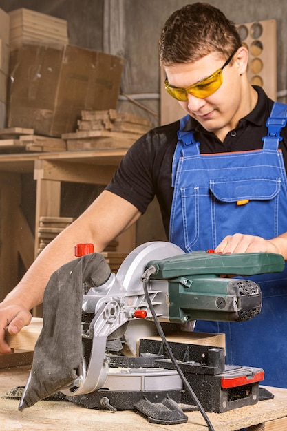 Young man builder carpenter sawing board with circular saw in workshop