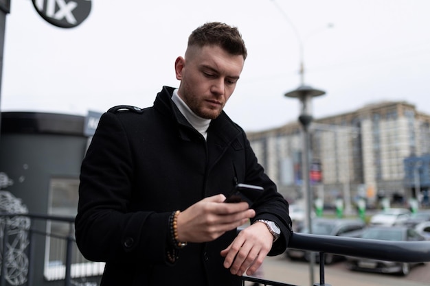 Young man in business clothes with a mobile phone in his hands outside