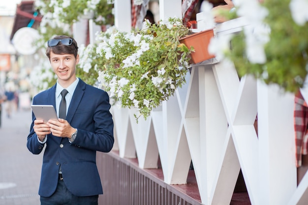 Young man in business suit holding tablet on summertime day