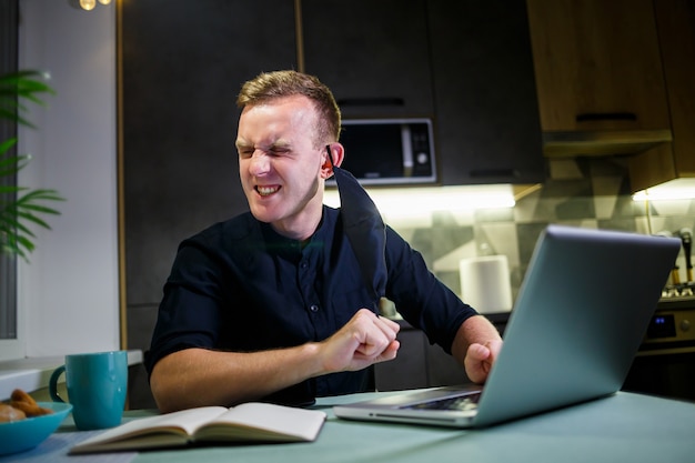 Young man businessman in a black anti-virus protective mask, working at home, sitting at the kitchen table with a laptop. Work at home in quarantine