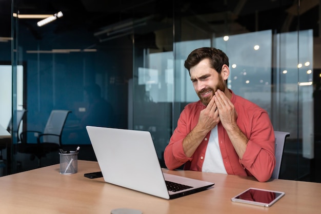 A young man businessman freelancer designer sits in the office at the table works on a laptop he