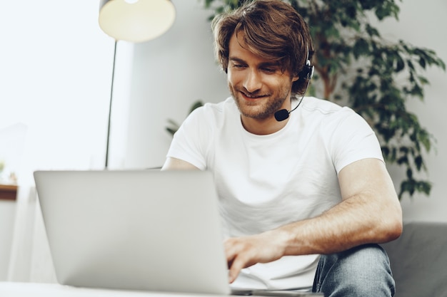 Uomo d'affari del giovane con la cuffia avricolare che lavora al computer portatile da casa