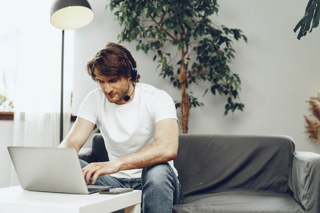 Молодой человек бизнесмен с гарнитурой работает на ноутбуке из дома