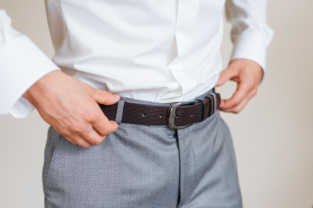 A young man buttons a brown belt on his trousers man's hands