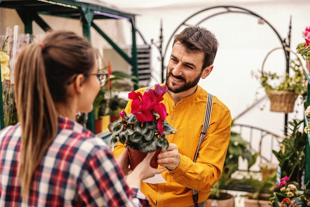 Young man buying flowers from nursery garden female worker.