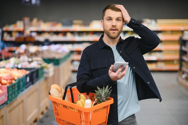 Молодой человек покупает продукты в супермаркете Другие покупатели на заднем плане Концепция потребительства