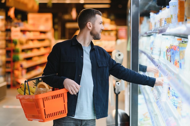 Молодой человек покупает продукты в супермаркете Другие покупатели на заднем плане Концепция потребительства