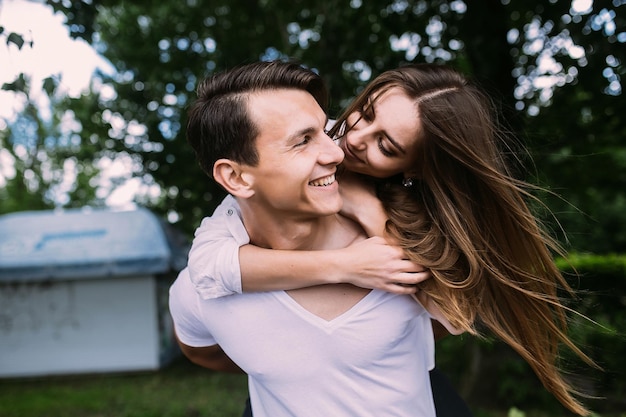 Young man carries his girlfriend on his back in the park