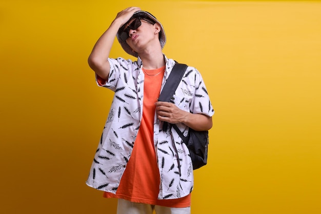 Young man carrying backpack on vacation gesturing forget something isolated on yellow background