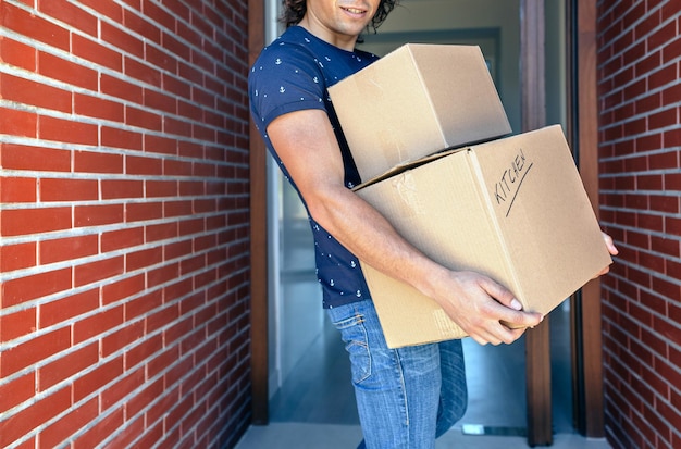 Photo young man carrying moving in cardboard boxes