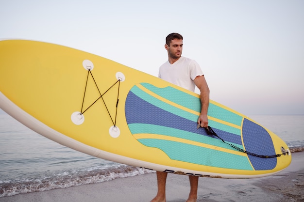 Young man carrying sup board after water surf session