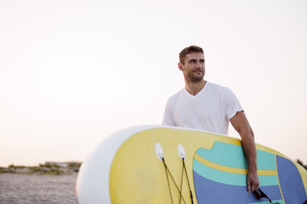 Young man carrying sup board after water surf session