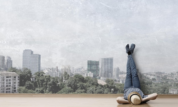 Young man in casual clothes and hat lying on the floor with legs raised up. Mixed media