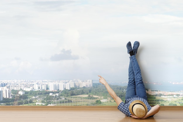 Young man in casual clothes and hat lying on the floor with legs raised up. Mixed media