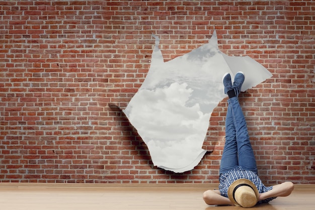 Young man in casual clothes and hat lying on the floor with legs raised up, torn paper effect on the wall. Mixed media