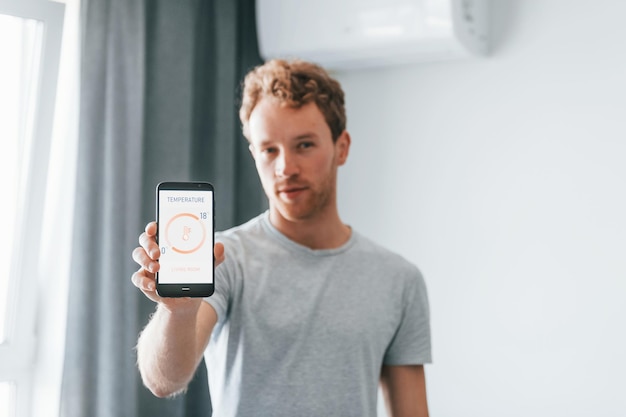 Young man in casual clothes is indoors controlling smart home technology