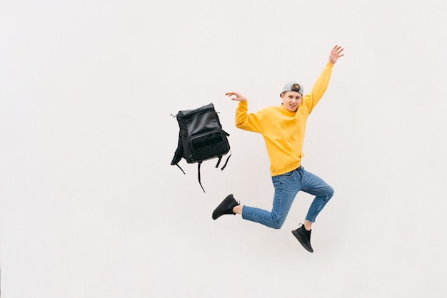 Young man in casual clothes jumps with a backpack