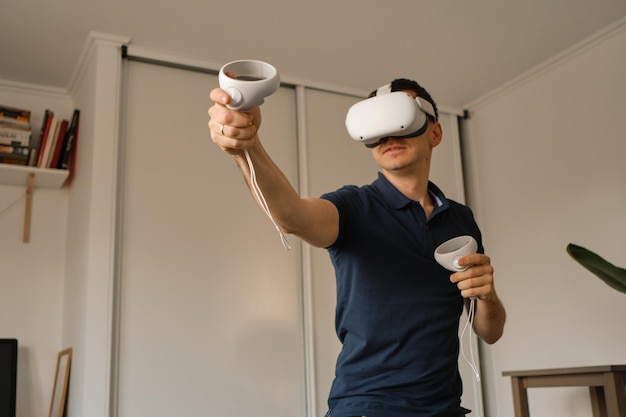 Young man in casual clothes plays virtual games at home Man in virtual reality VR helmet compensates