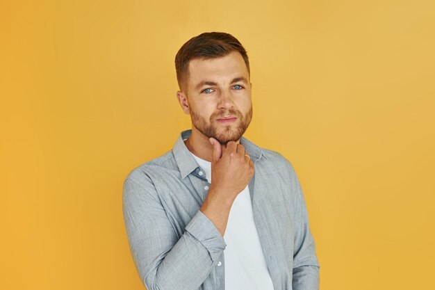 Young man in casual clothes standing indoors in the studio and demonstrates emotions