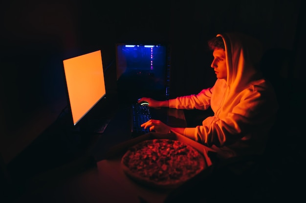 빨간 스크린 피자 상자가 있는 컴퓨터와 함께 밤에 작업하는 캐주얼 옷을 입은 젊은 남자