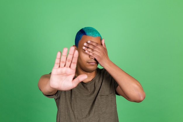 Young man in casual on green wall cover his eyes with hands showing stop gesture