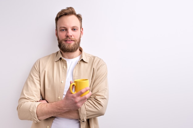 Young Man In Casual Wear Posing At Camera Holding Yellow Mug on White wall